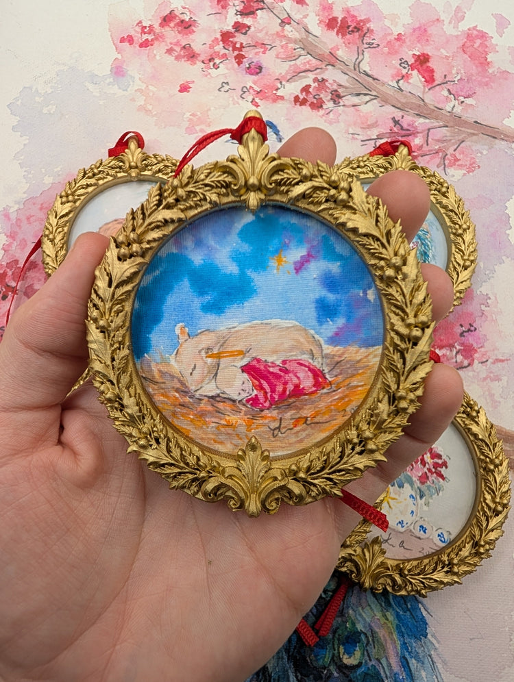 Baby Jesus and the Lamb watercolor ornament in a gold wreath frame, held in hand