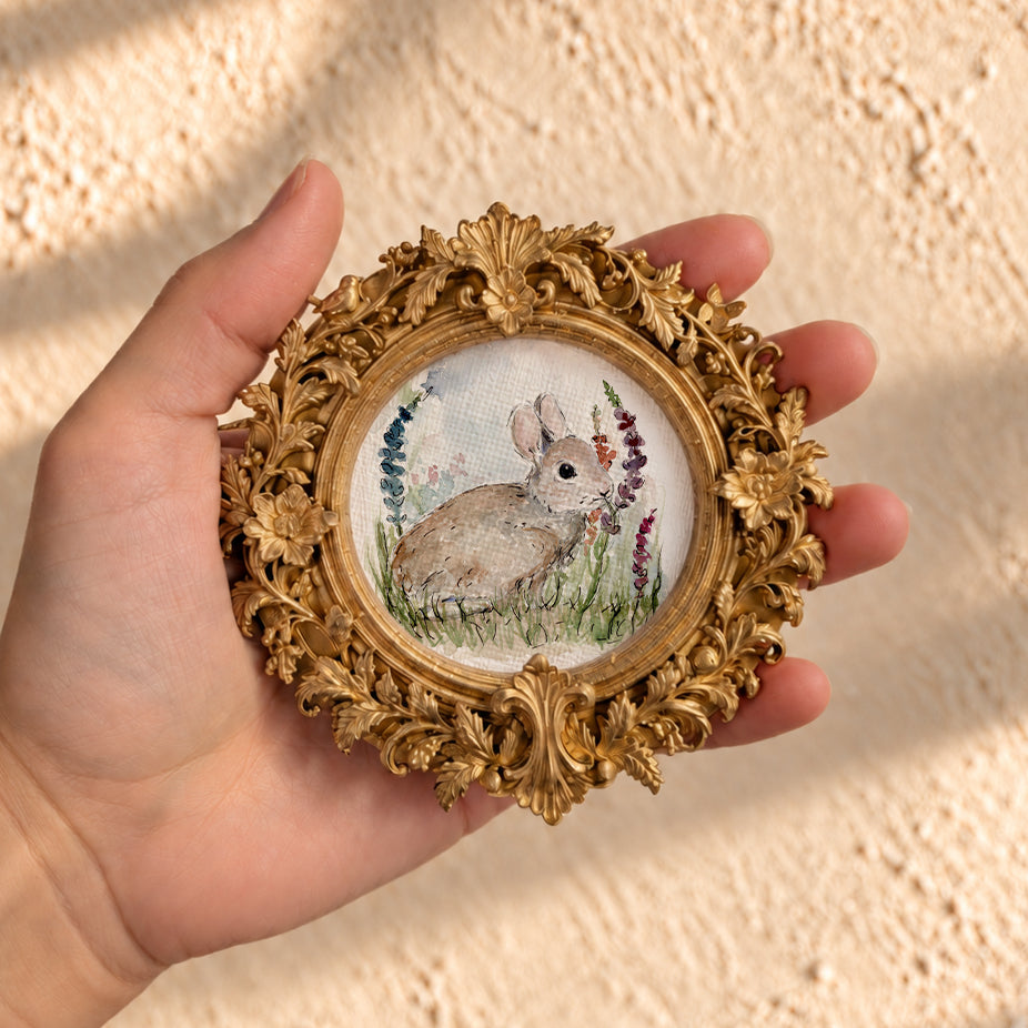 Baby bunny watercolor print in round gold baroque frame, held in hand