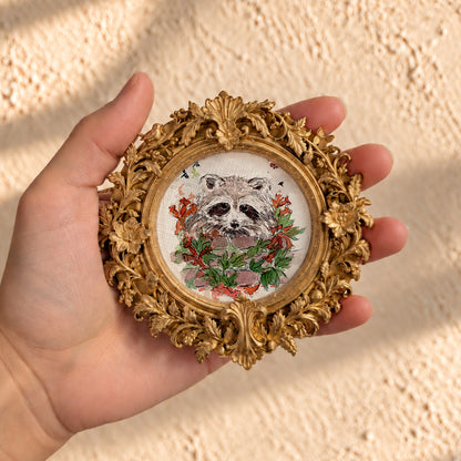 Baby raccoon watercolor print in round gold baroque frame, held in hand