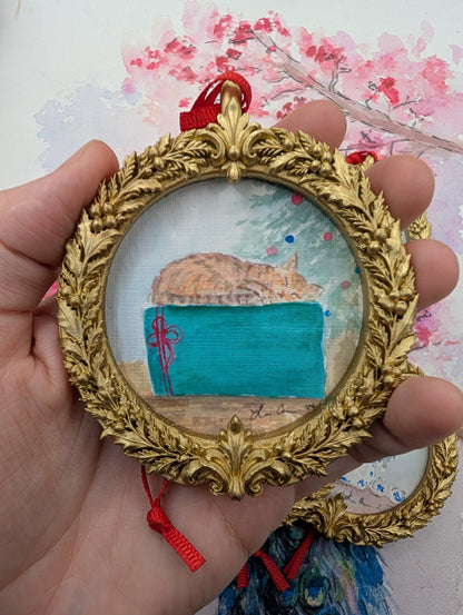 Tabby Cat and Teal Gift watercolor ornament in a gold wreath frame, held in hand