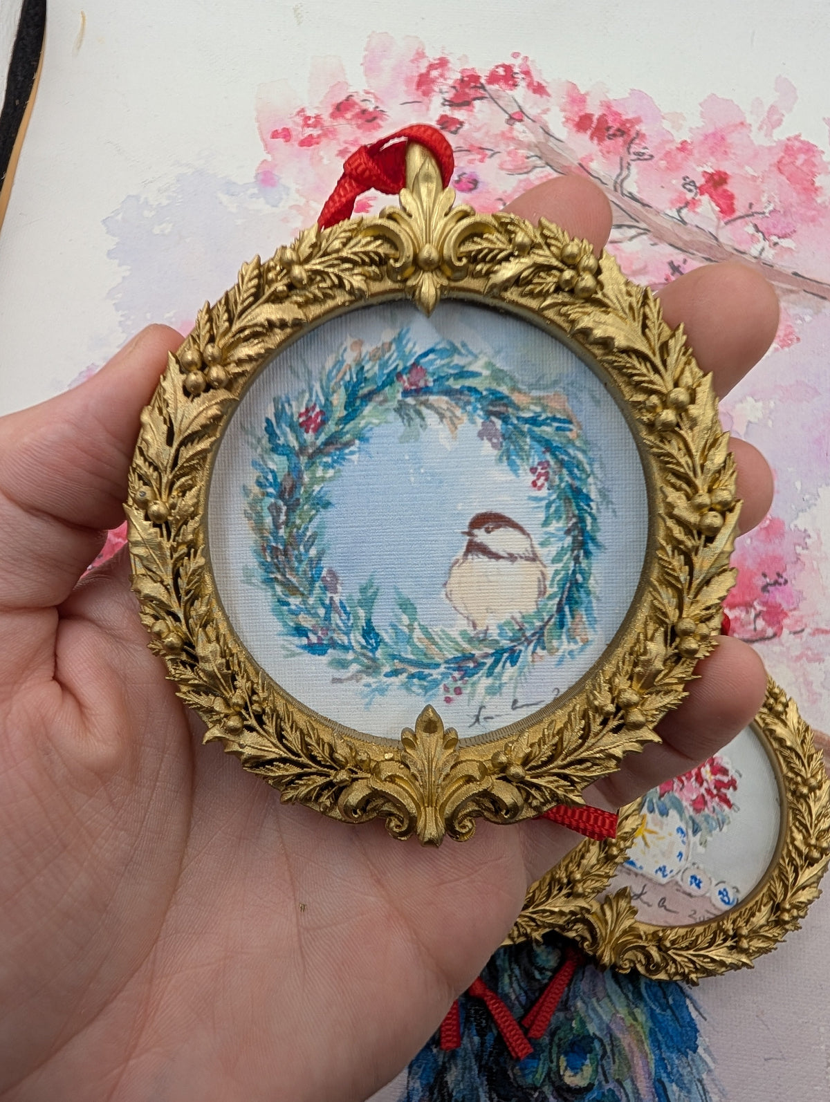 Chickadee in a Winter Wreath watercolor ornament in a gold wreath frame, held in hand